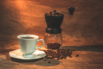 White cup of coffee with coffee grinder in the background. Rustic wood background. With grains scattered around