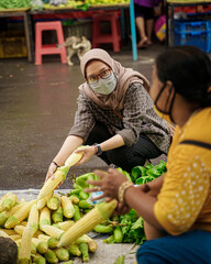 Muslim women wearing health cloth masks while in traditional markets shopping for vegetables.