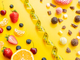 Fresh fruits vs sugar sweets divided by measurement tape on yellow