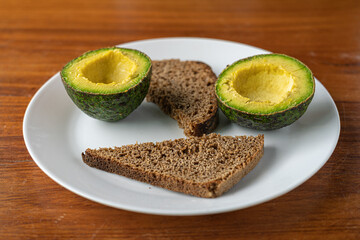 Close up fresh avocado cut in half and slices of bread on white plate on wooden table