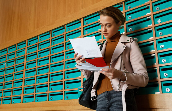 Attentive woman taking out mail from mailboxes in entrance