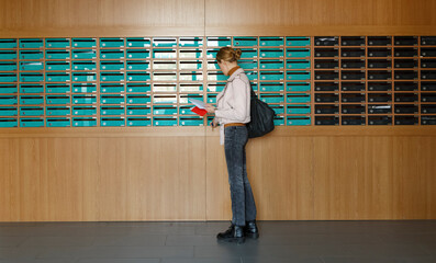 Calm woman with bag taking out mail from mailboxes in entrance
