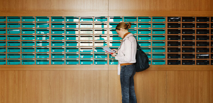 Attentive woman taking out mail from mailboxes in entrance