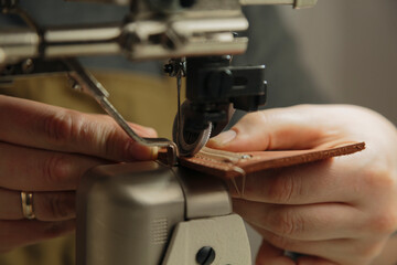 Tailor diligently sewing leather on sewing machine under lamp