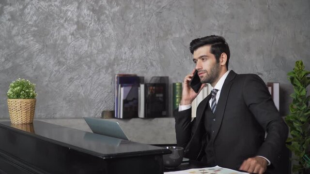 Footage B roll A Cheerful guy is working in office making mobile phone call and using laptop taking notes in notebook. Business communication. Work from home , business technology concept. 