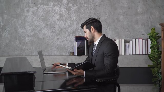 Footage B roll A Cheerful guy is working in office making mobile phone call and using laptop taking notes in notebook. Business communication. Work from home , business technology concept. 