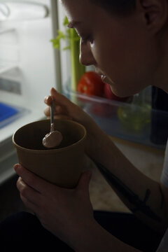 Woman eating unhealthy food near fridge