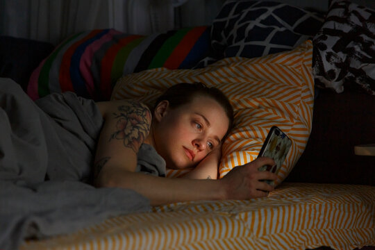 Tattooed woman lying in bed and using mobile phone