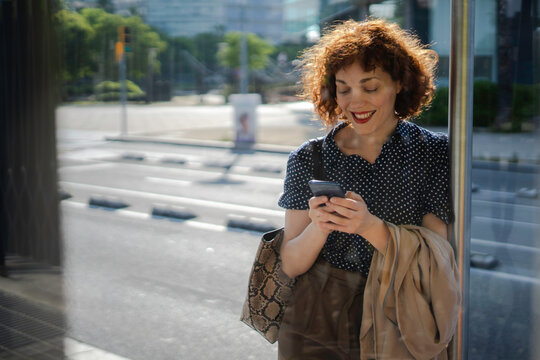 Woman typing on her phone while standing at bus station alone