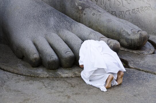 Jain pilgrim is praying at the feet of the gigantic statue of Gomateshwara in Sravanabelagola, Karnataka, India, Asia