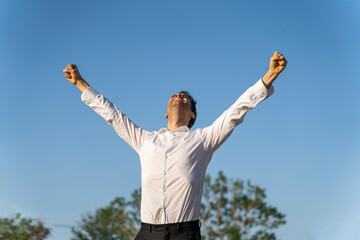 Successful businessman with arms raised standing against clear blue sky