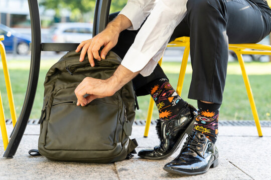 Male entrepreneur wearing colorful socks zipping backpack while sitting on chair at sidewalk cafe
