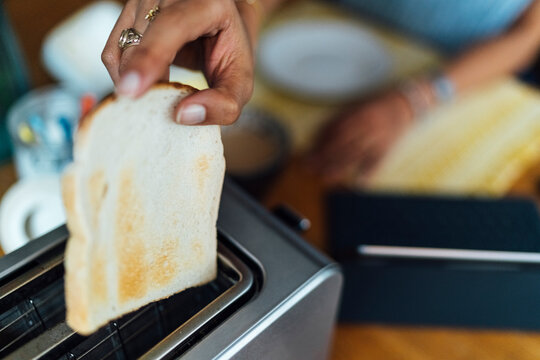 Close-up of young woman hand placing bread in toaster
