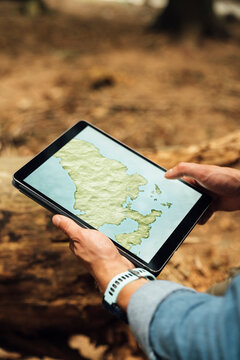 Close-up of man's hands analyzing map over digital tablet in forest