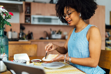 Young woman with curly hair buttering bread on table at home