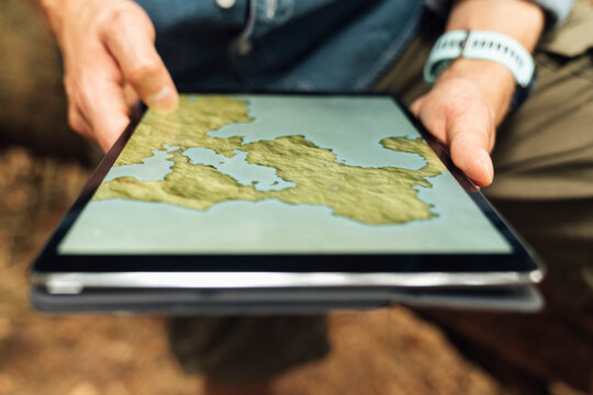 Close-up of male hiker's hands using map over digital tablet in forest