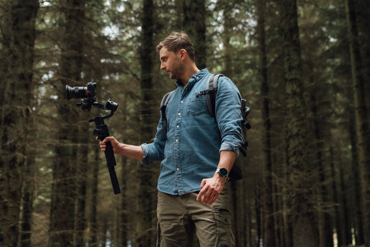 Man filming with camera and gimbal while standing against trees in forest