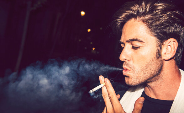 Close-up of mid adult man smoking cigarette outdoors at night