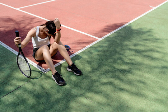 Sad female tennis player sitting on floor in sports court