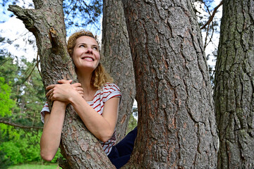 Thoughtful woman embracing while sitting on tree in forest