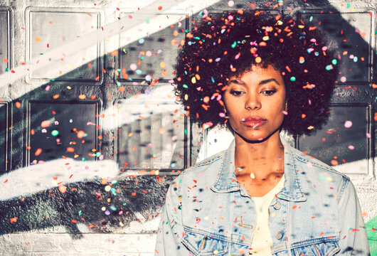 Confetti falling on thoughtful woman looking down while standing against wall