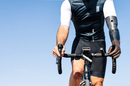 Male amputee athlete with artificial hand cycling against clear blue sky - Powered by Adobe