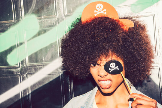 Close-up of woman clenching teeth while holding fake pirate eye patch against wall
