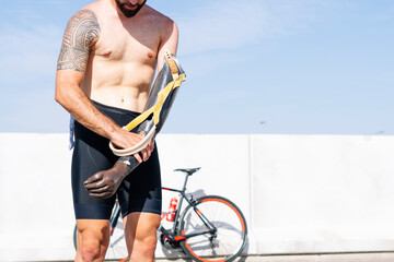 Shirtless male athlete wearing artificial hand while standing against clear sky on sunny day