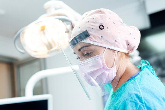 Dentist in protective workwear looking down while standing at clinic