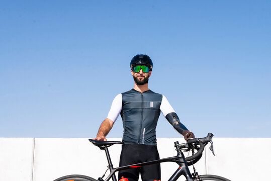 Male amputee cyclist with bicycle standing against clear blue sky