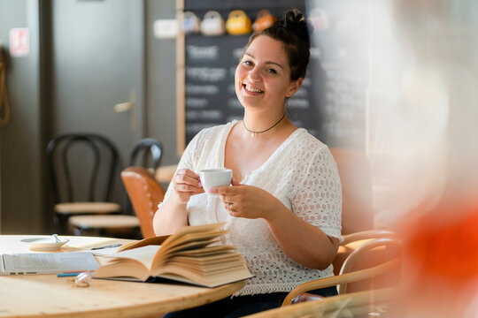 Smiling voluptuous woman holding coffee cup while sitting at table in restaurant
