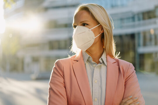 Blond female entrepreneur wearing protective face mask while looking away in financial district during coronavirus