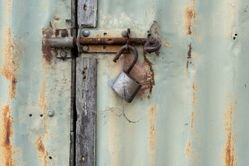 Old rusty open lock on a green coloured, rusty corrugated iron shed door. 