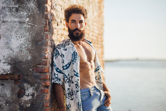 Young bearded man standing with shirt open against brick wall