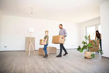 Father and son carrying cardboard boxes while walking on hardwood floor in new house