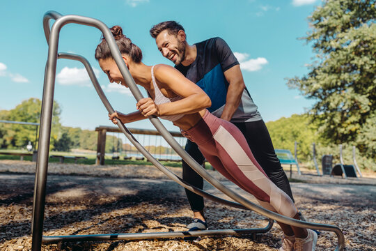 Man supporting woman doing press-ups on a fitness trail