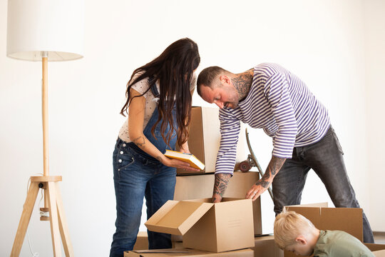 Family unpacking cardboard boxes against wall in new house