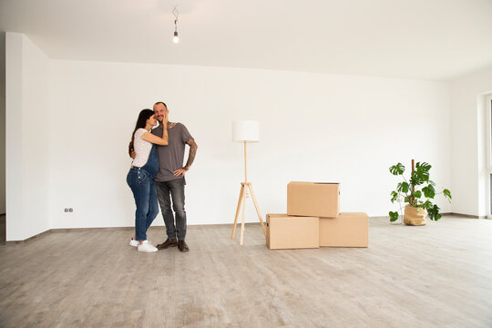 Romantic couple standing by electric lamp and boxes standing against wall in new apartment