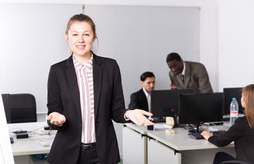 Elegant young businesswoman politely welcoming to modern open plan office