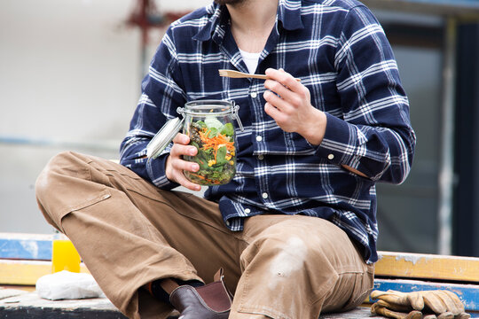 Close-up of construction worker holding salad in jar while sitting outdoors at site