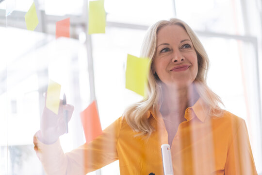 Businesswoman looking away while planning over adhesive notes stuck on window in home office