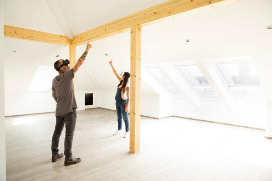 Couple looking through virtual reality simulators while standing in attic of new home