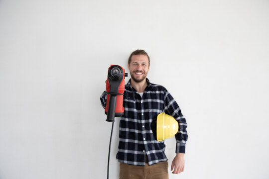 Smiling male worker holding work tool and helmet while standing against wall in house