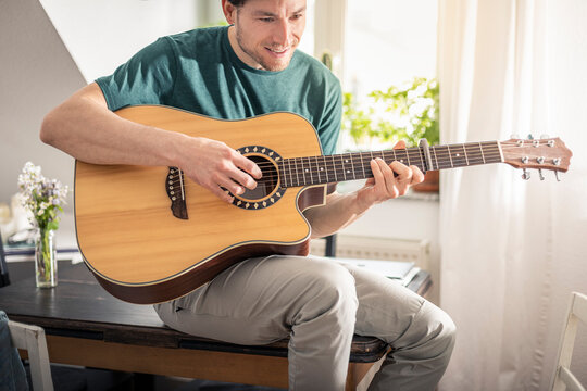 Smiling man playing guitar while sitting on table at home