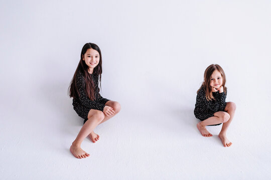 Smiling sisters sitting against white background in studio