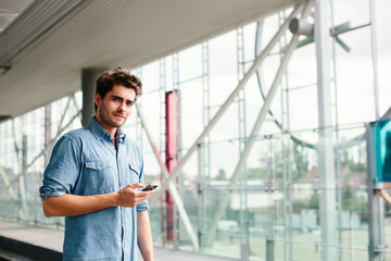 Confident casual businessman using smart phone while standing ta railroad station