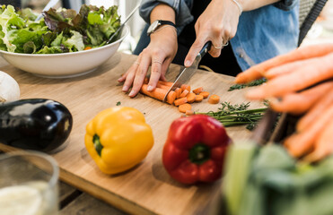 Close-up of young woman chopping carrots on cutting board
