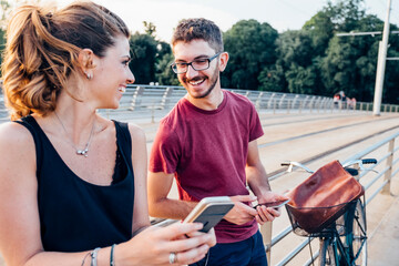 Happy couple using smart phones while standing on bridge at sunset