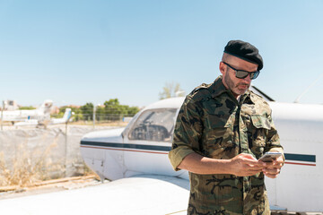 Army soldier text messaging on smart phone against sky