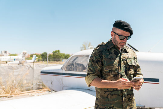 Army soldier text messaging on smart phone against sky